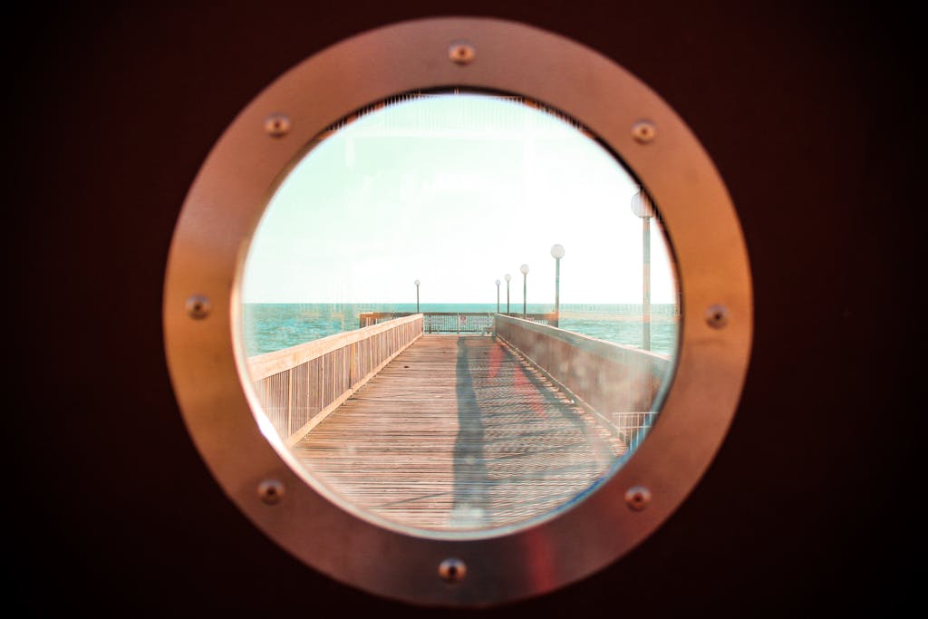 Darlnaija Captivating view of a wooden pier extending into the ocean through a round window.