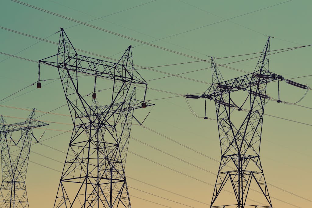 Utilities of high voltage power lines against a twilight sky, illustrating energy infrastructure.