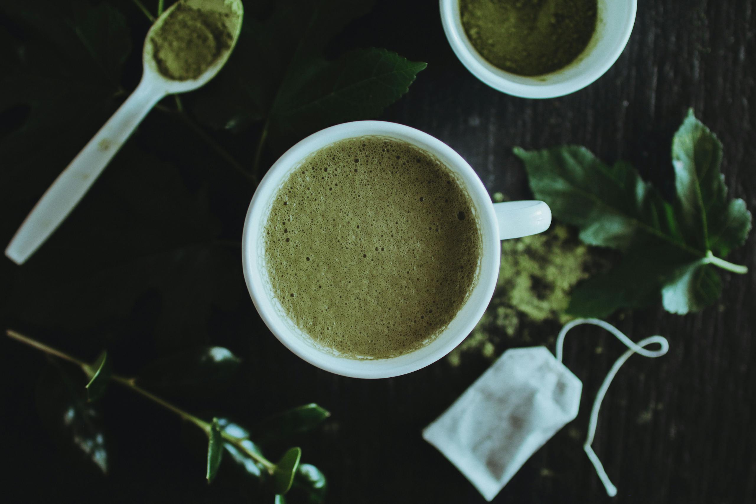 Bin Matcha A calming overhead shot of a matcha latte surrounded by leaves and matcha powder for a natural touch.
