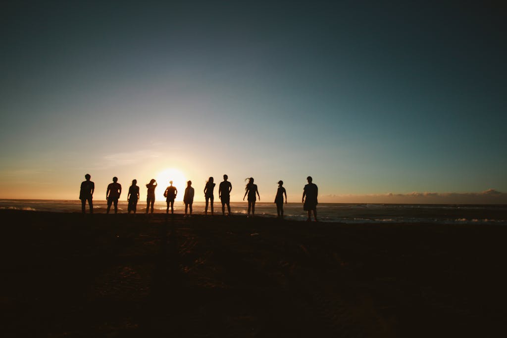 JuntosSeguros A group of friends standing on a beach, silhouetted against a vibrant sunset over the ocean.