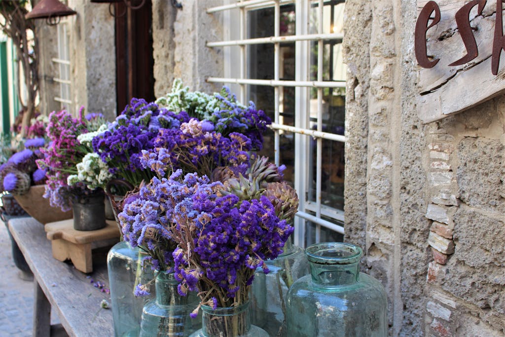 Shop Spring Vase A vibrant and rustic outdoor display of purple and blue flowers in glass vases.