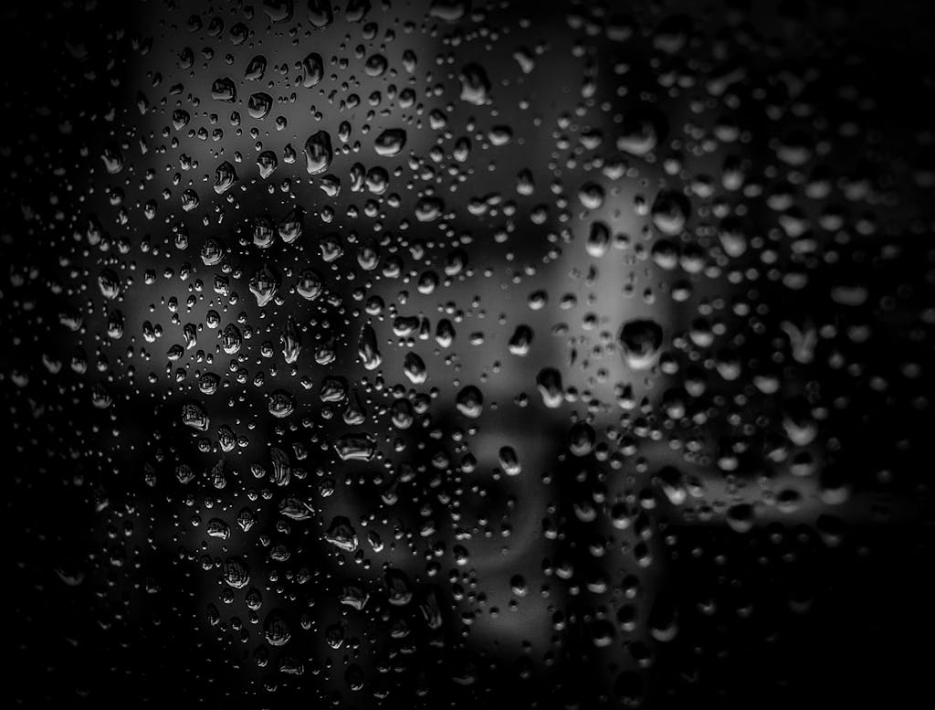 Cray0lav0mit Close-up of raindrops on a glass surface with a dark background, creating an abstract and moody effect.