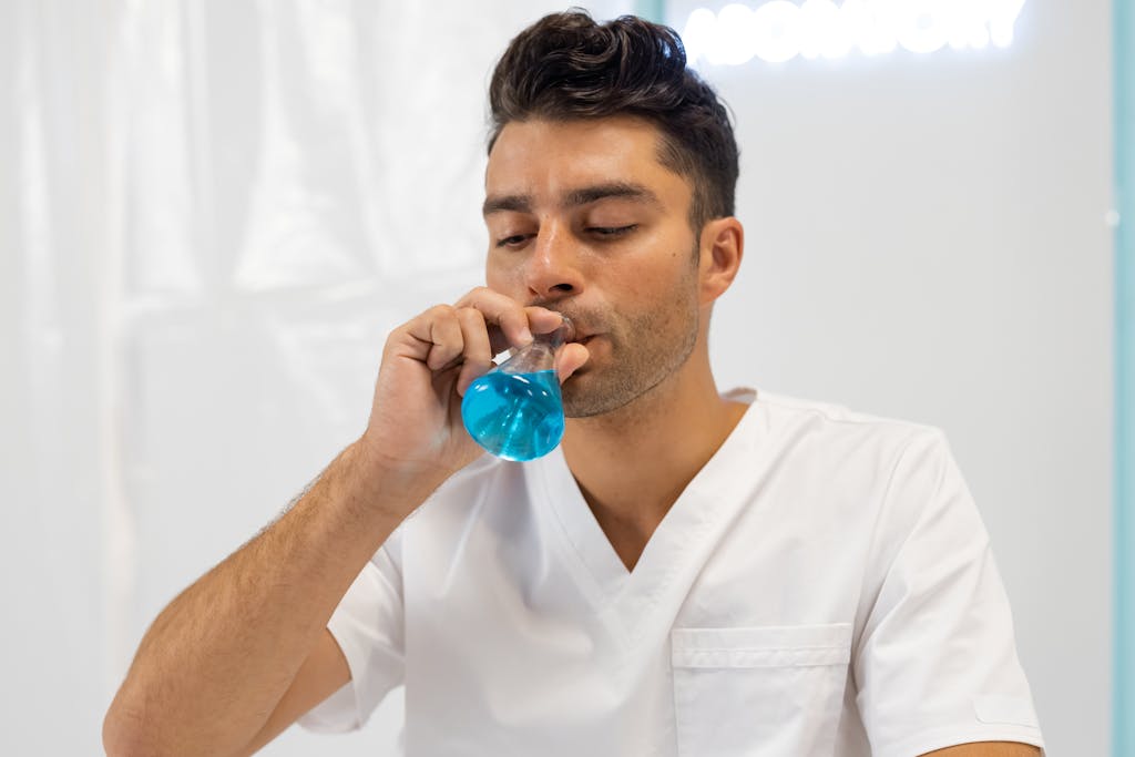 Bottlecrunch Man in a lab coat drinks blue liquid from a flask, focusing on experimental research.