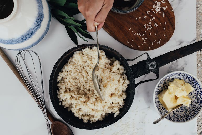 Dampfreis Overhead view of rice being cooked in a frying pan with butter and utensils.