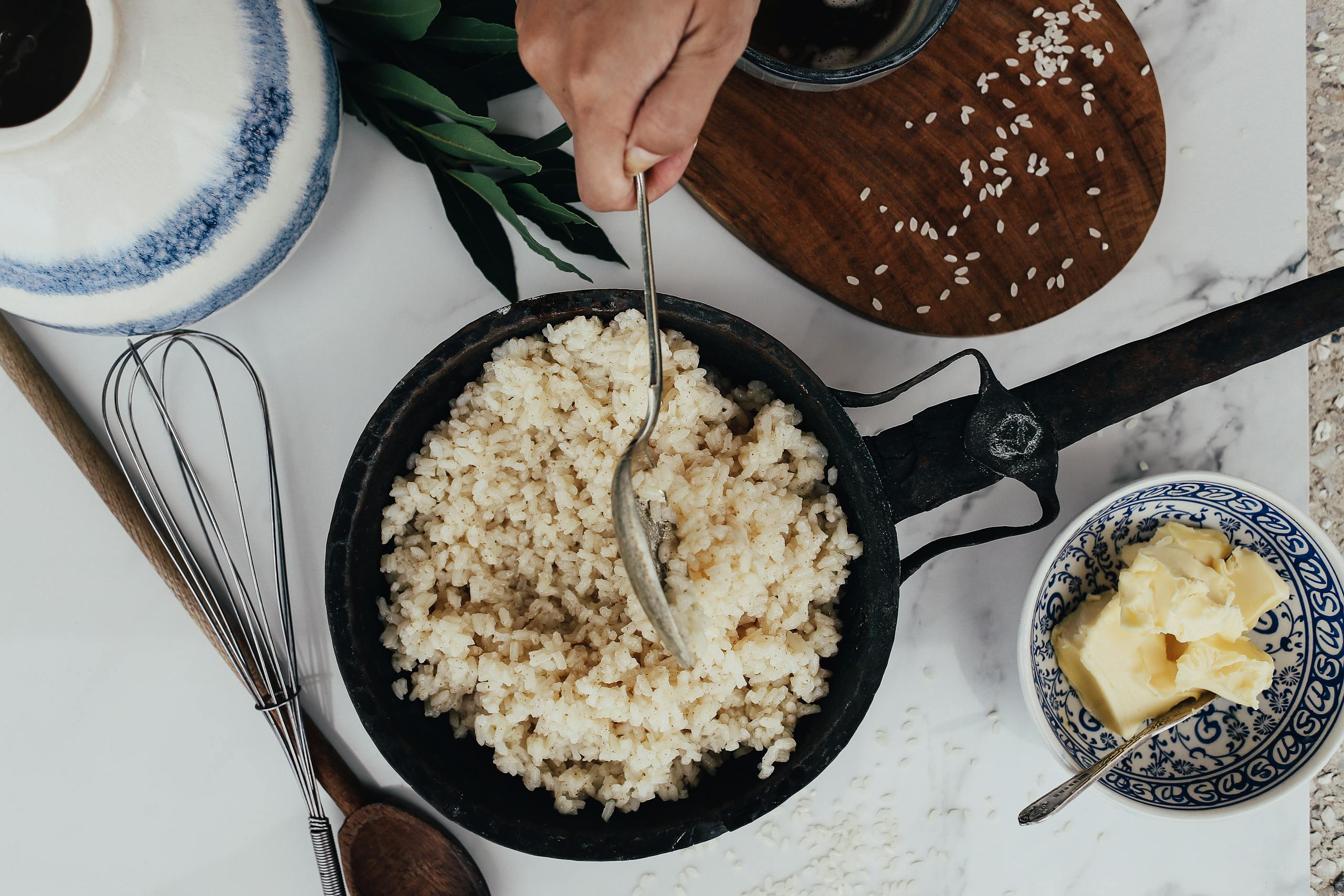Dampfreis Overhead view of rice being cooked in a frying pan with butter and utensils.