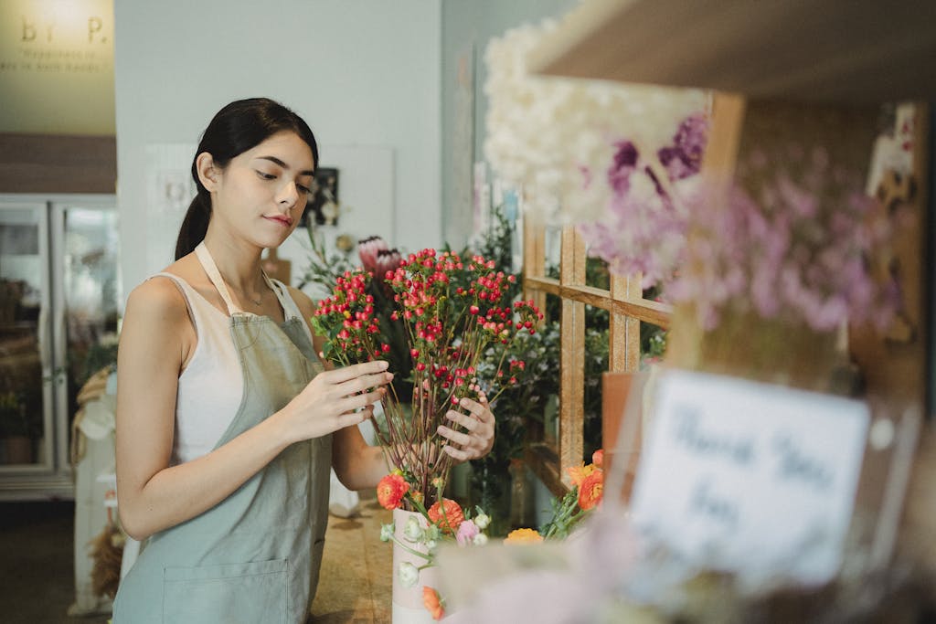 Shop Spring Vase Positive female florist with dark hair making composition of small red flowers while preparing order during work in floristry studio