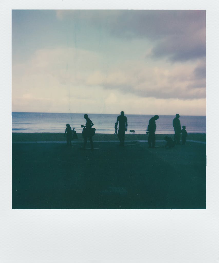 JuntosSeguros Silhouettes of people enjoying a serene evening at the beach, captured in vintage instant film style.