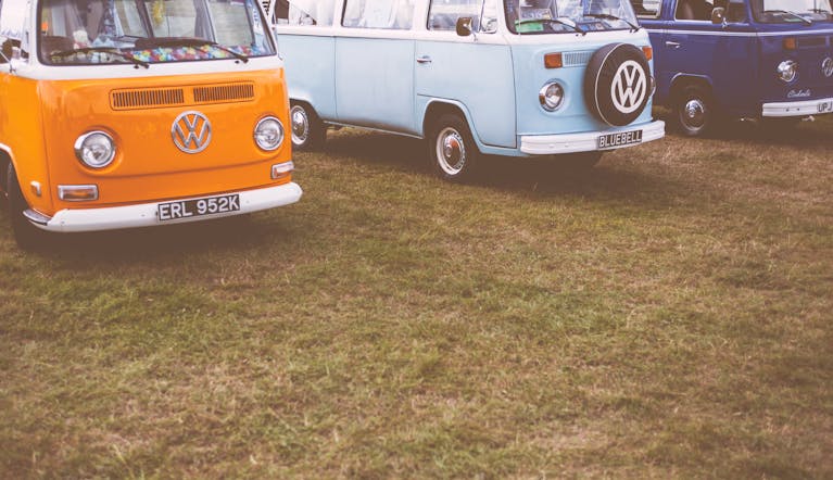 Messeregge Three vintage Volkswagen vans in orange, blue, and navy, parked on grassy field.