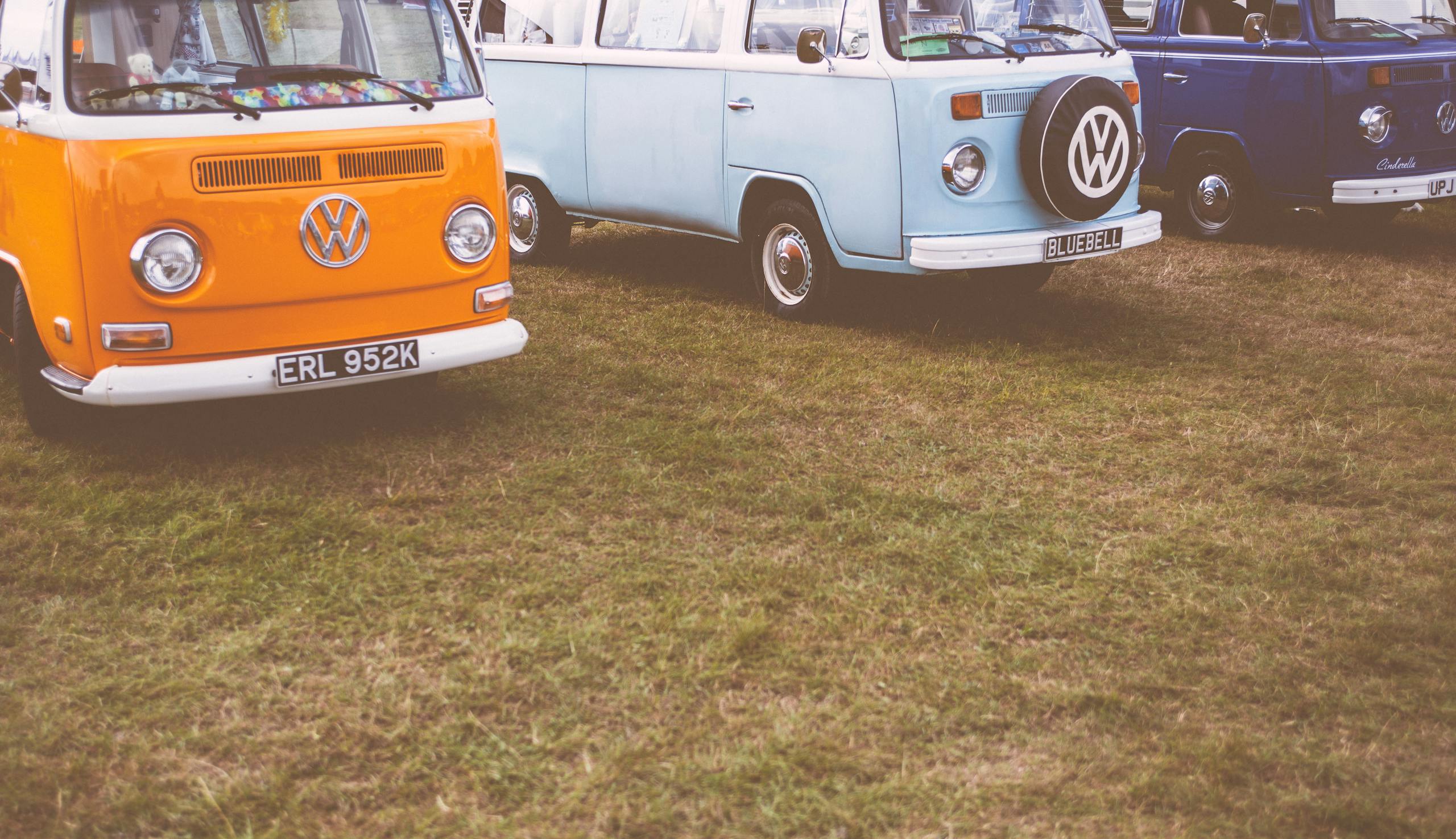 Messeregge Three vintage Volkswagen vans in orange, blue, and navy, parked on grassy field.