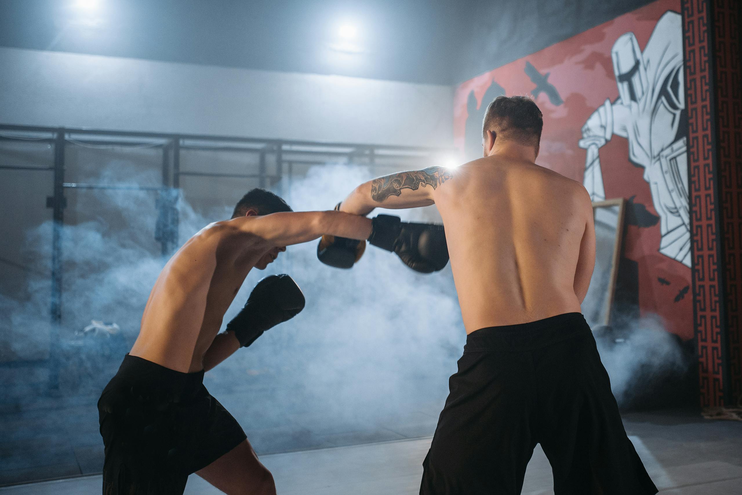 Slylar Box Two shirtless men sparring in a smoky gym setting, showcasing powerful boxing techniques.