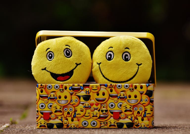 JuntosSeguros Two yellow smiley plush toys in an emoji-themed box, expressing fun and happiness.